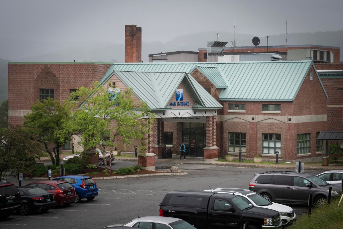 A brick and metal-roofed building on a cloudy day, with parked cars in the foreground and trees surrounding the structure.