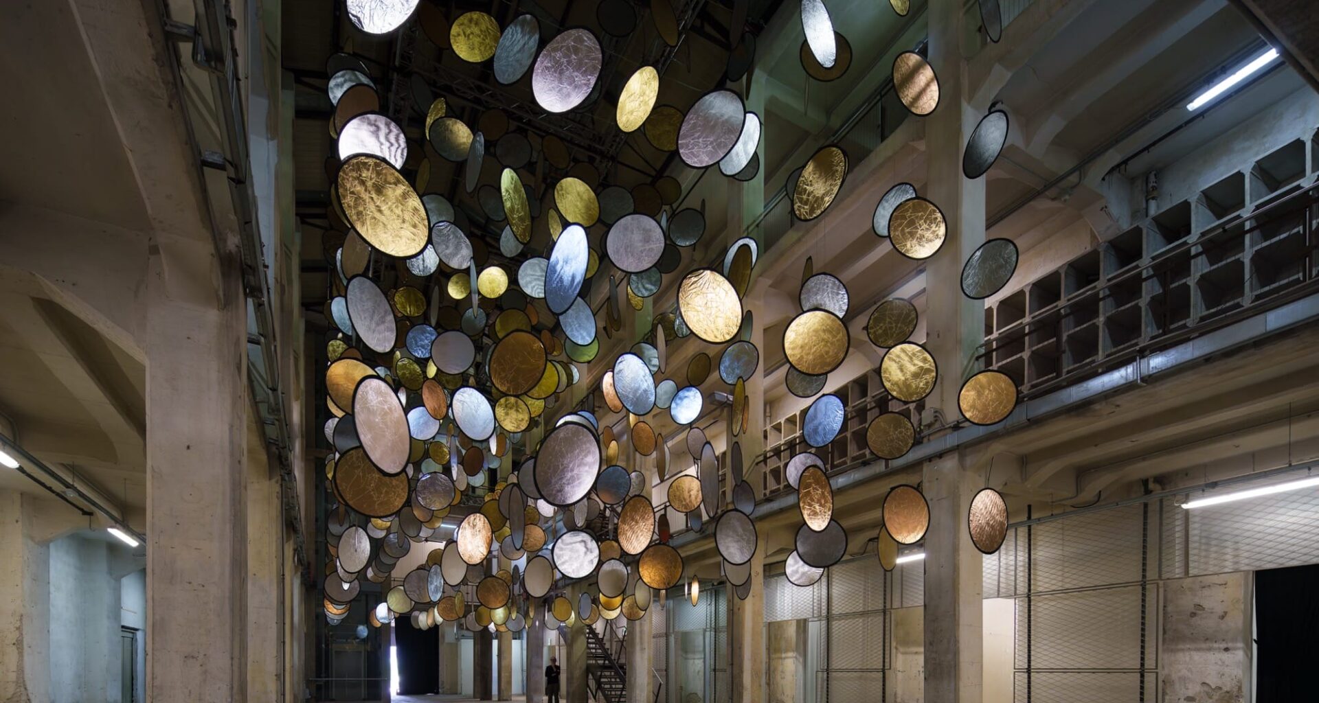 A large interior installation of metallic discs hanging from the ceiling in an industrial space