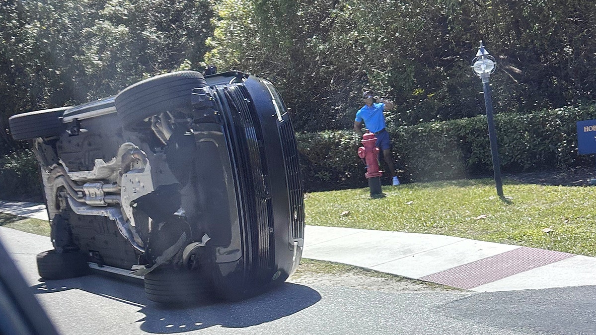 Golfer Tiger Woods stands next to his overturned vehicle on a roadside in Jupiter Island, Fla.