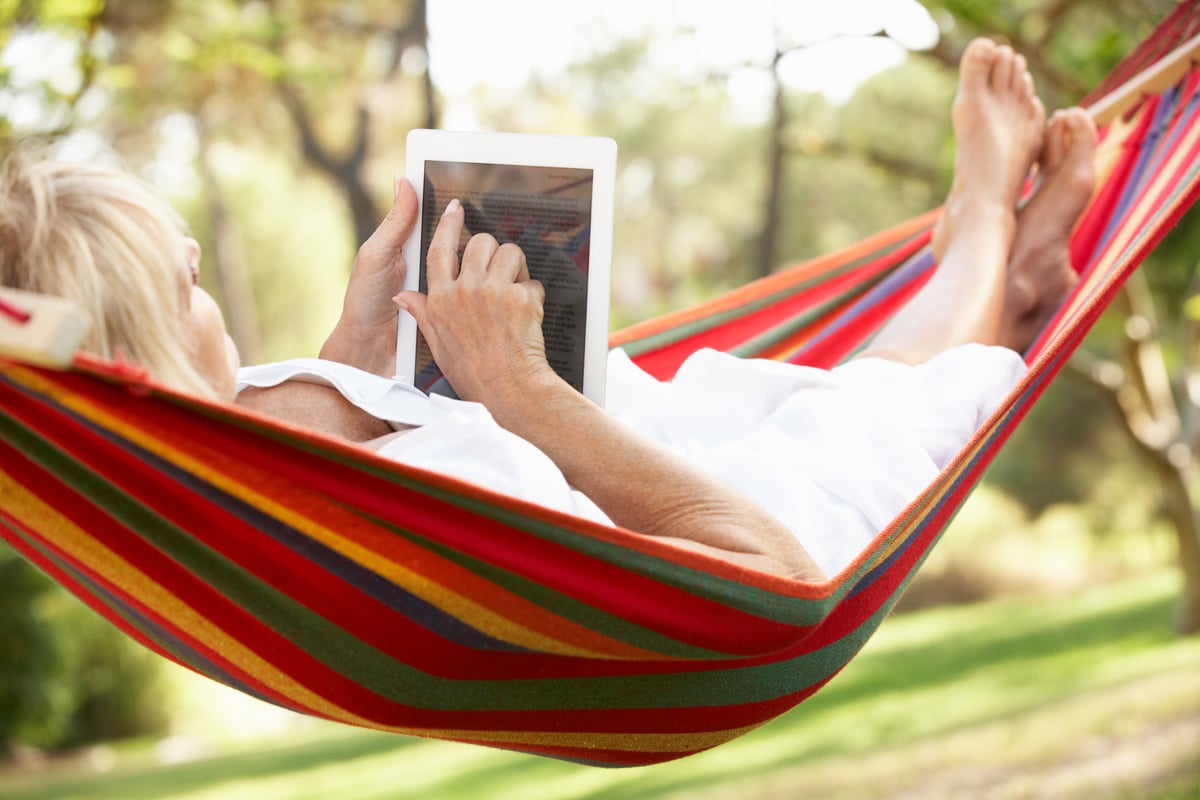 Someone reading a tablet while in a hammock.