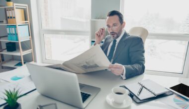 A slightly surprised-looking person reads a newspaper while sitting in an office.