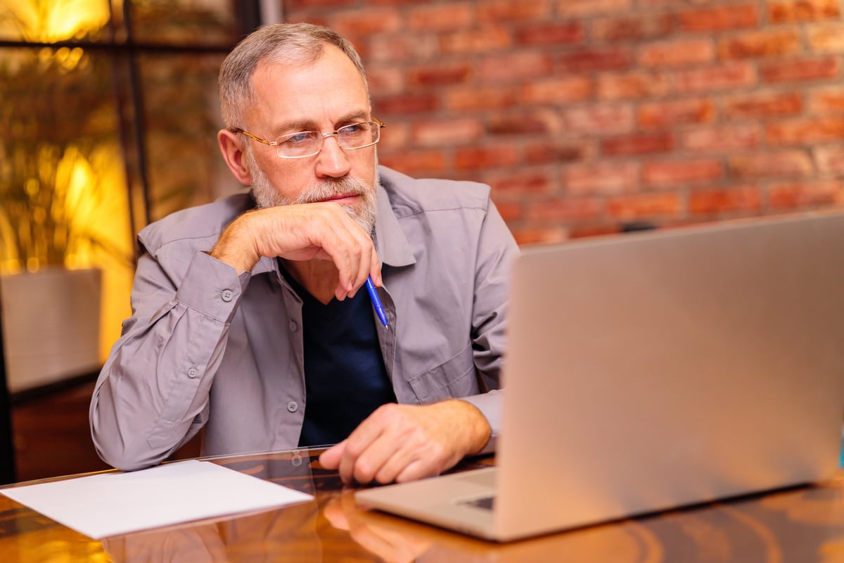 Serious person staring at laptop screen and holding pen.