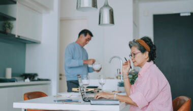 Couple in kitchen together, one using a laptop.