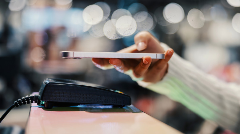 Person making tap to pay purchase with smartphone