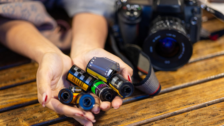 Someone holding 35mm film rolls in their hand with a camera nearby.