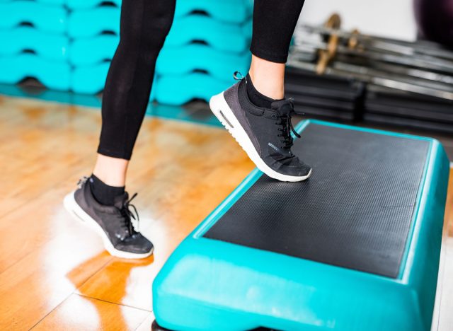 Fit Brunette Girl with Black Shoes, Black Legging and Blue and Yellow Sports Outfit and Shirt at the Gym working on her Fitness