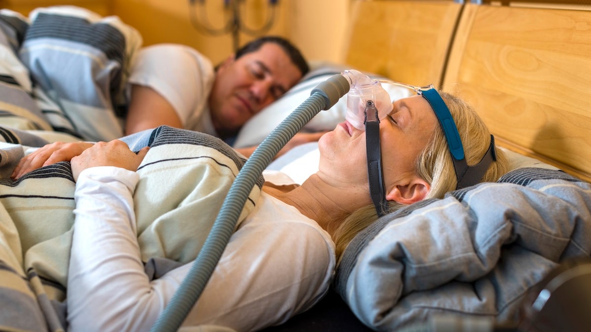 Woman using CPAP machine with husband holding her hand beside her