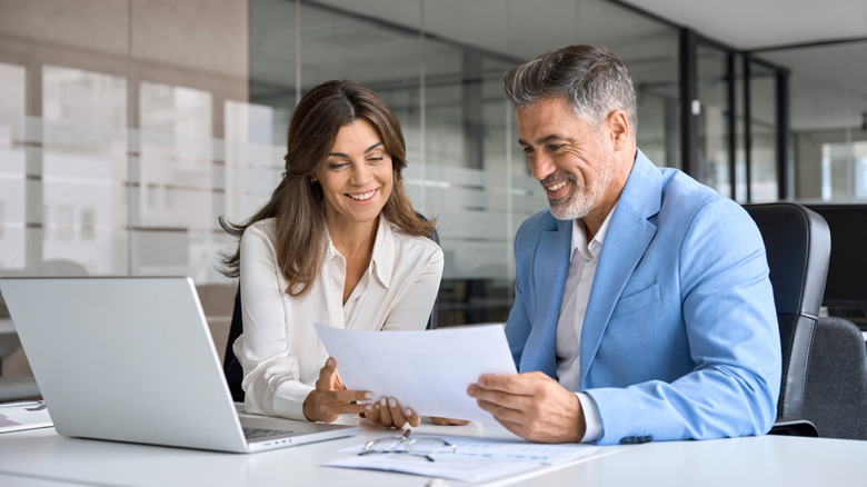Two middle-aged business professionals smiling while looking at paper
