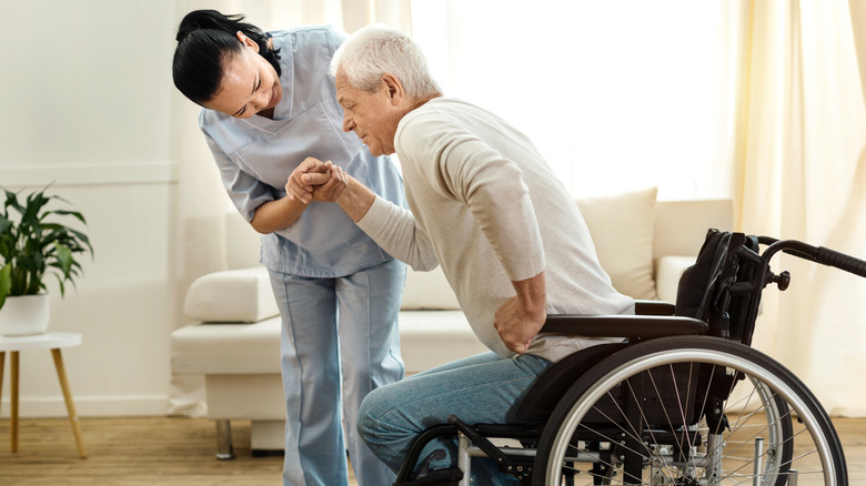 A senior man being helped out of his wheelchair by a nurse in his home.