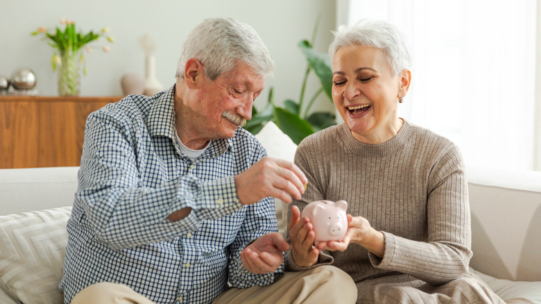 A happy mature couple placing a coin into a piggy bank.