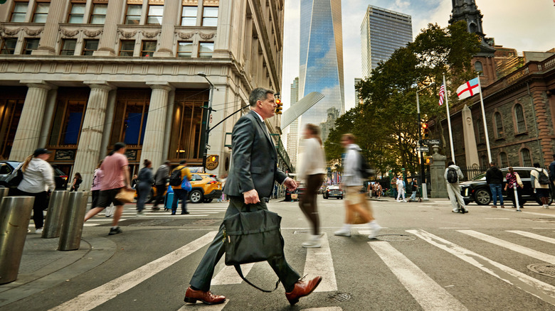 A mature man in a suit crossing the street in New York and walking in the opposite direction of everyone else