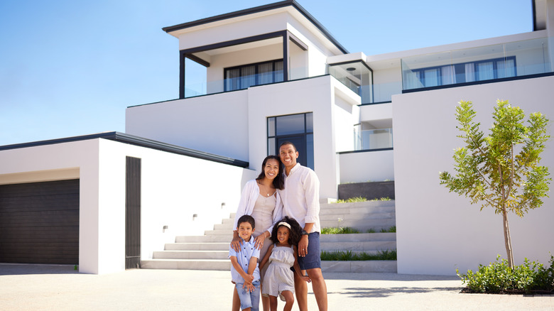 A smiling family standing outside in front of a luxury home on a sunny day.