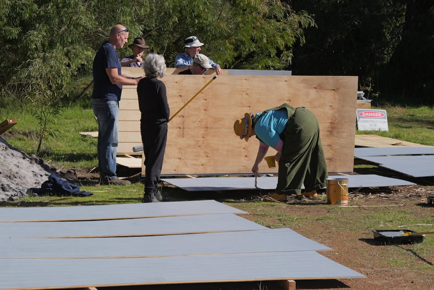 Four people paint wood panels and two people watch on.