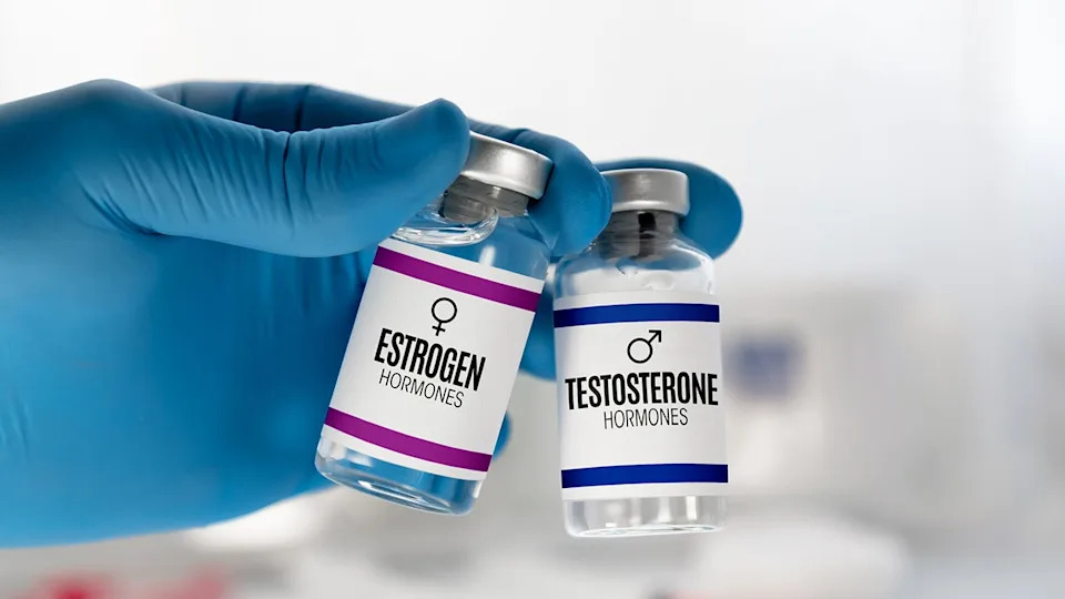 Hand of doctor holding two injection vials labeled testosterone and estrogen