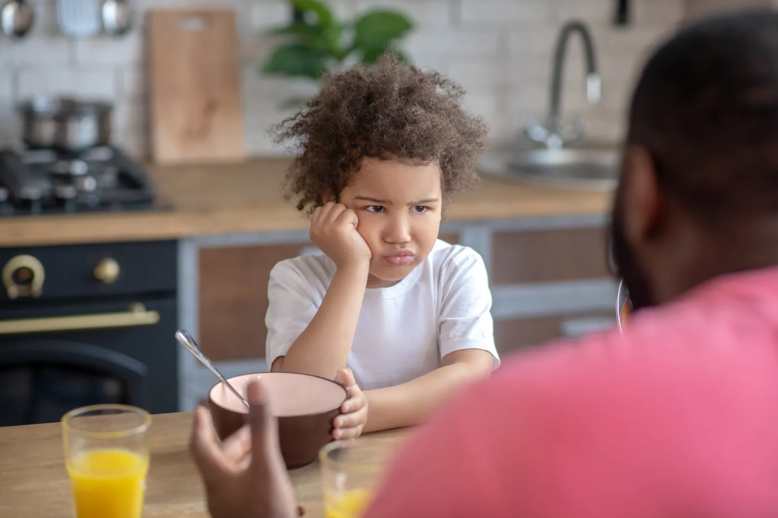A stock photo showing a little girl staring at her father and looking sad, not wanting to eat.