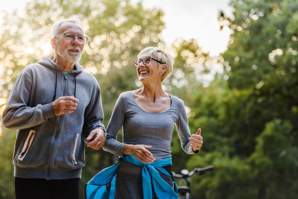 A smiling senior couple jogging in a park.