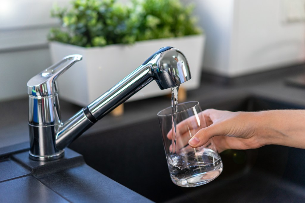 A woman's hand fills a glass with tap water in a kitchen sink.
