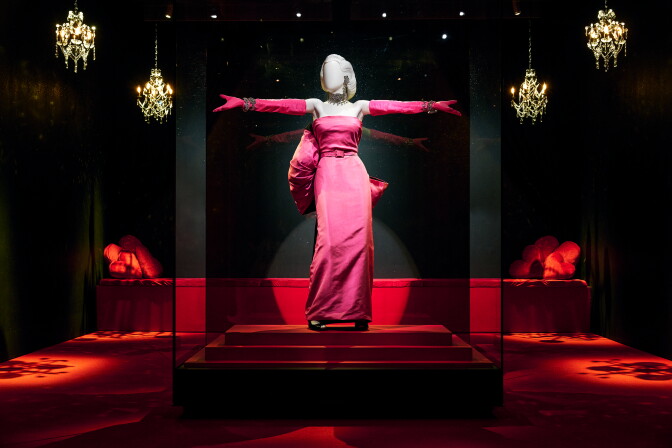 A mannequin with its arms out to the side wears pink gloves and a pink dress.
