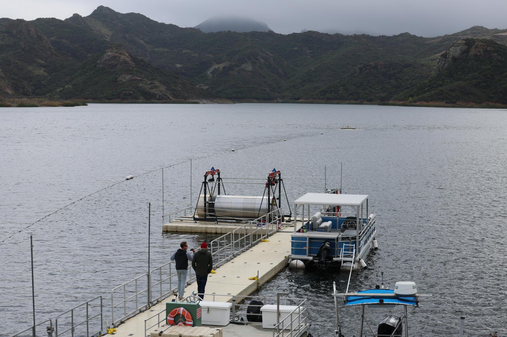Two people walk on a dock toward an OceanWell desalination device during testing at Las Virgenes Reservoir.