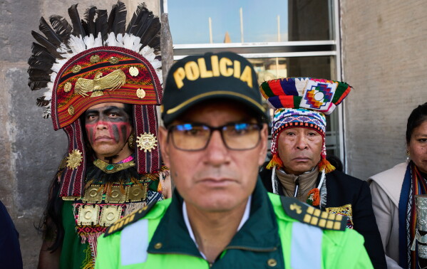 A police officer stands guard next to Indigenous men shortly before the arrival of presidential candidate Roberto Sanchez, of the Together for Peru party, at the airport to welcome him with an Indigenous ceremony, in Cusco, Peru, Tuesday, June 2, 2026. (AP Photo/Rodrigo Abd)