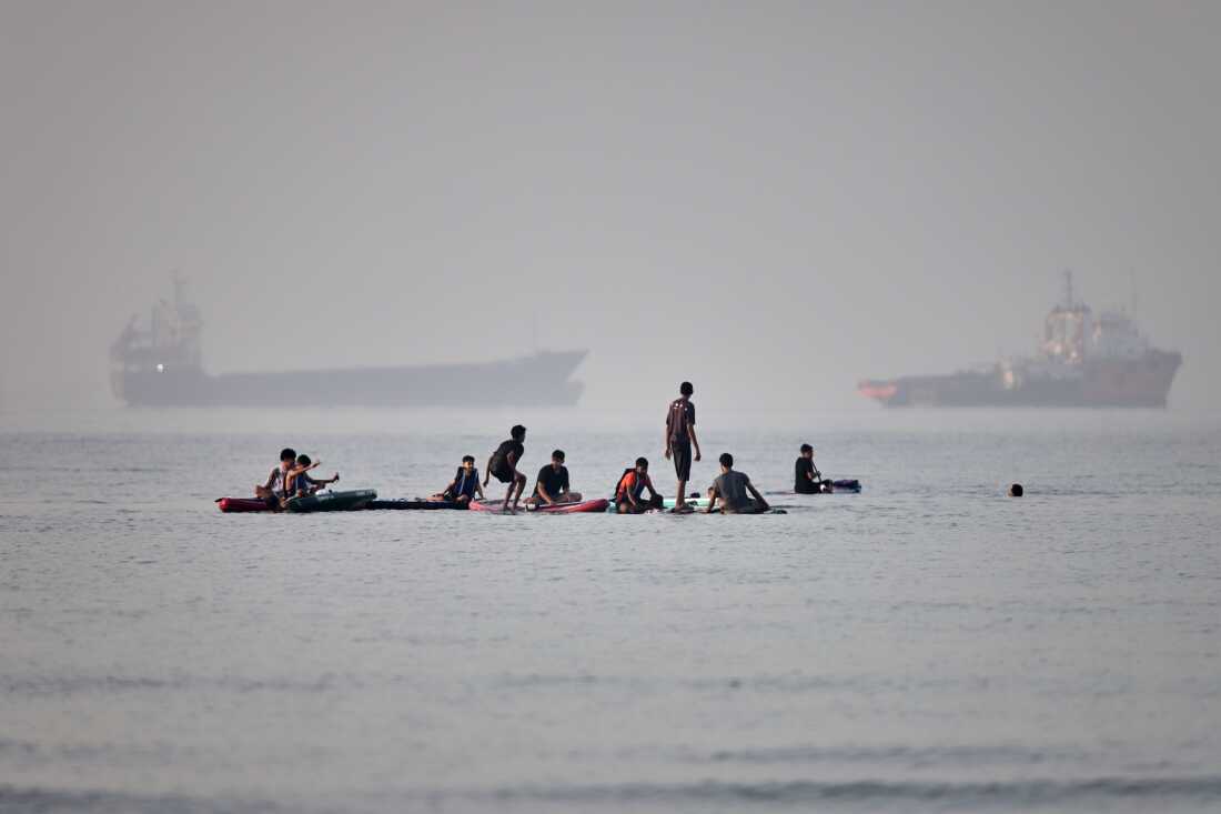 People gather on paddleboards in shallow water as cargo and service vessels are anchored in the Strait of Hormuz off Bandar Abbas, Iran, Monday, June 1, 2026.