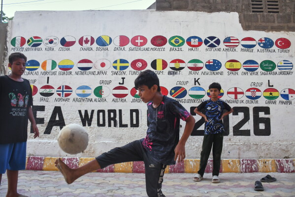 Children play soccer next to a wall painted with the flags of countries participating in the 2026 FIFA World Cup, in Lyari, a neighbourhood of Karachi, Pakistan, Wednesday, June 3, 2026. (AP Photo/Ali Raza)