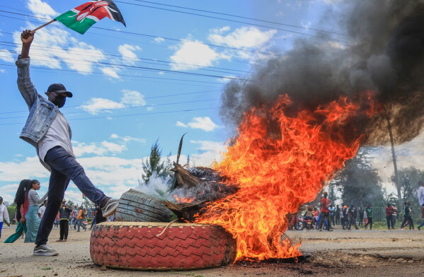 A protester raises a Kenyan flag near a burning barricade during a demonstration against a proposed Ebola quarantine center to be established by the United States at Laikipia Air Base in Nanyuki, Kenya, Monday, June 1, 2026. (AP Photo/Andrew Kasuku)