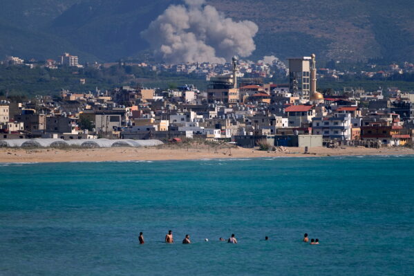 People swim on a public beach as smoke, background, rises from an Israeli airstrike that hit the Qlaileh village, seen from the southern port city of Tyre, Lebanon, Tuesday, June 2, 2026. (AP Photo/Mohammed Zaatari)