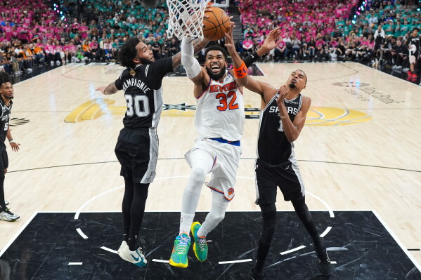 New York Knicks center Karl-Anthony Towns (32) shoots between San Antonio Spurs forward Victor Wembanyama (1) and forward Julian Champagnie (30) during the first half of Game 1 of the NBA Finals basketball series, Wednesday, June 3, 2026, in San Antonio. (AP Photo/Eric Gay)