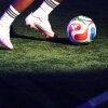 Detail of the FIFA World Cup 2026 match ball "Trionda" at Brooklyn Bridge Park in New York City on October 2, 2025. A pair of feet wearing white soccer cleats appears near the white, red, blue and green soccer ball.