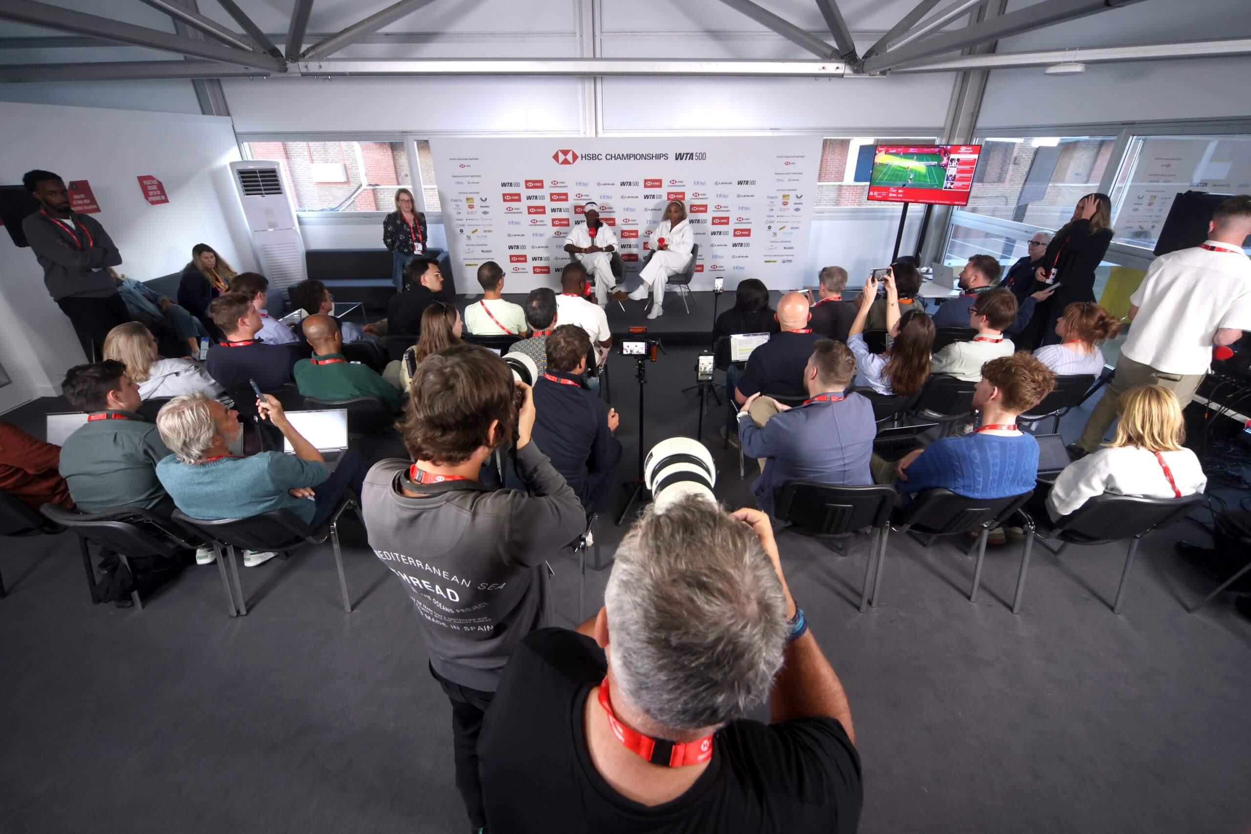 A general view of photographers and journalists at a news conference, with Victoria Mboko (left) and Serena Williams (right) sitting on a stage.