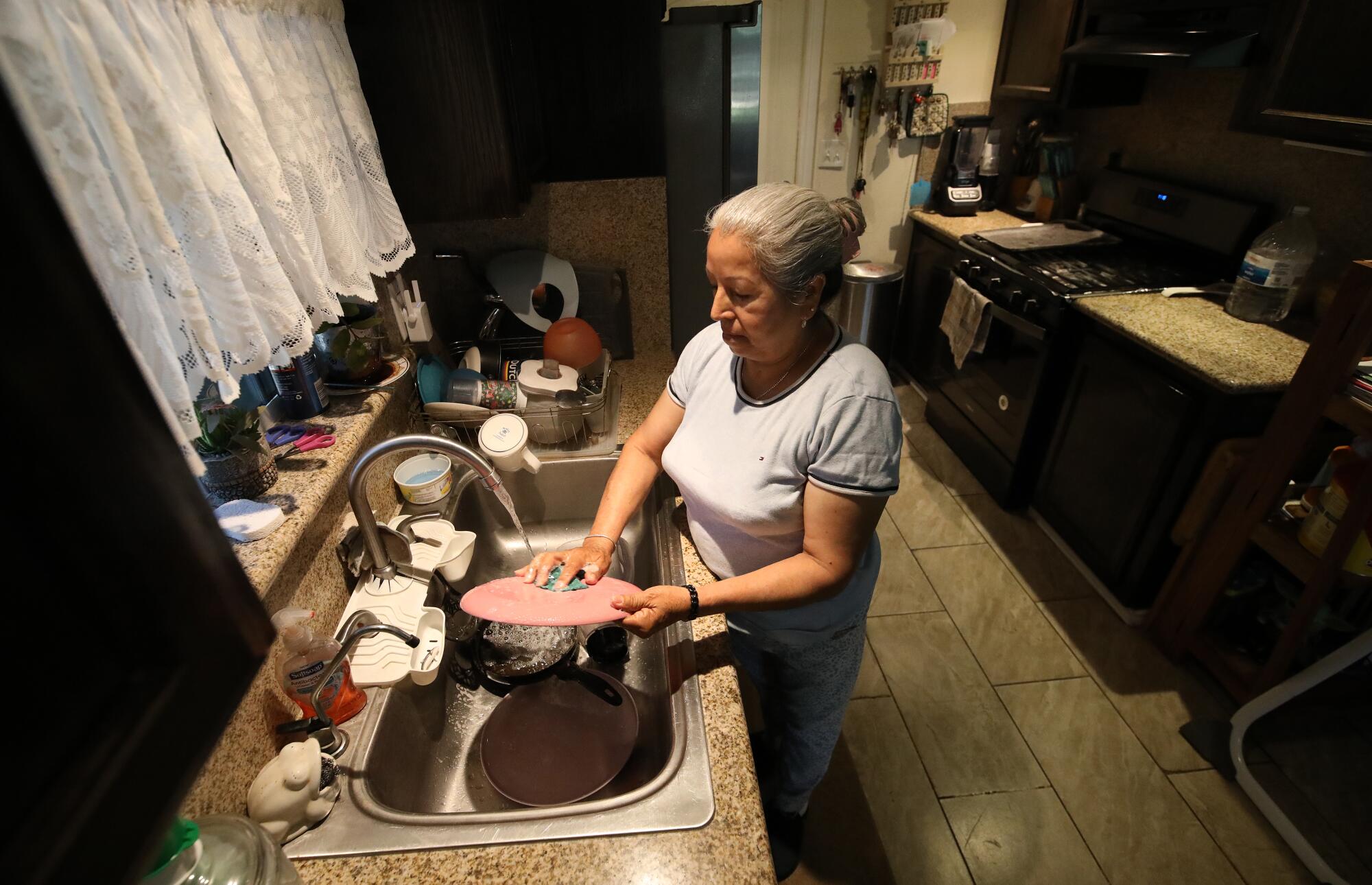 A woman washes dishes at her kitchen sink