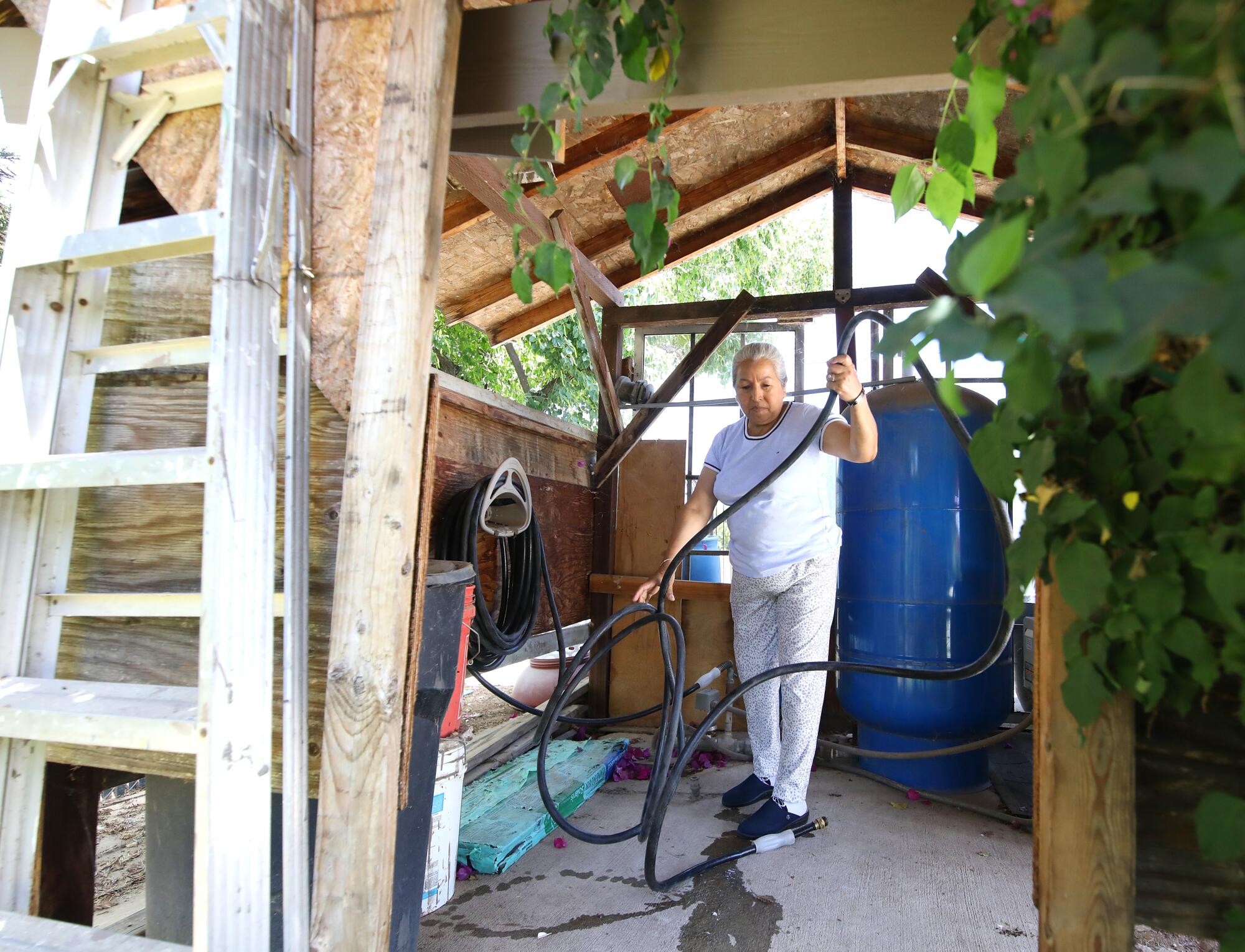 A woman dealing with a hose in a shed, with a large blue tank behind her