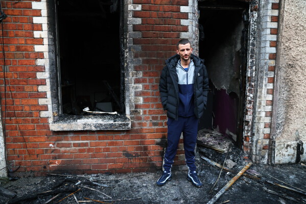 Jamie Corrie stands beside his burnt out house after rioting broke out late Tuesday, in east Belfast, Northern Ireland, Wednesday, June 10, 2026, following a stabbing incident. (AP Photo/Peter Morrison)