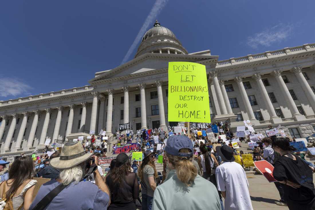 Protesters hold signs in front the of the Utah State Capitol building to oppose the construction of the Stratos data center on May 23, 2026 in Salt Lake City, Utah. The most prominent sign in the photo reads: "DON'T LET BILLIONAIRES DESTROY OUR HOME!"
