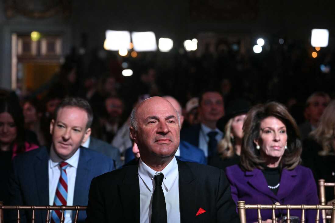 Canadian businessman and media personality Kevin O'Leary (C) looks on before US President Donald Trump speaks about 'Trump Accounts' at the Andrew W. Mellon Auditorium in Washington, DC, on January 28, 2026. He is wearing a black suit, white dress shirt and black tie.
