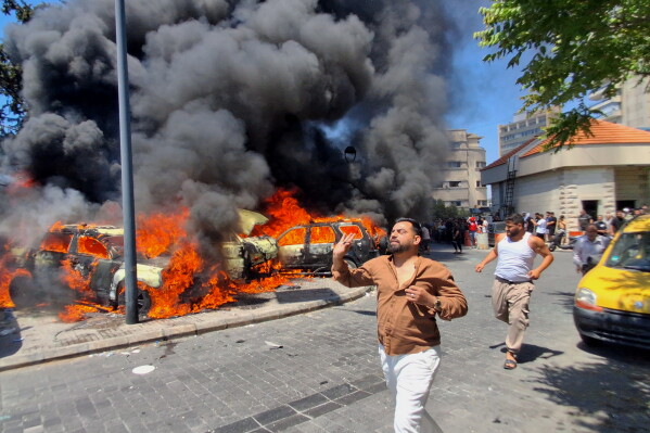 People run in front of burned cars that were attacked in an Israeli airstrike in the southern port city of Sidon, Lebanon, Wednesday, June 10, 2026. (AP Photo/Mohammed Zaatari)
