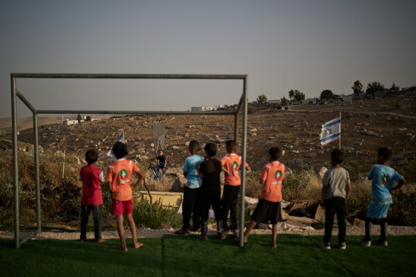 Palestinian boys look toward a young Israeli settler after their soccer ball, kicked beyond a barbed-wire fence surrounding a small football pitch near the Carmel settlement, was taken away in the West Bank Bedouin village of Umm al-Khair, Tuesday, May 12, 2026. (AP Photo/Leo Correa)