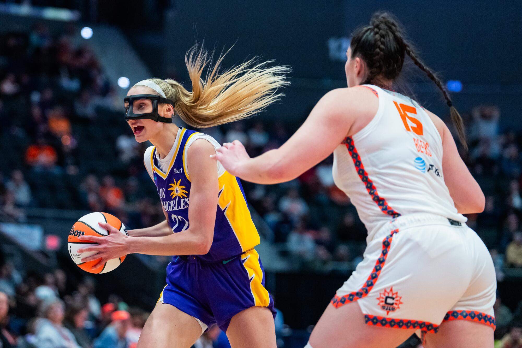 Sparks forward Cameron Brink, wearing a facemask, controls the ball while defended by Sun forward Raegan Beers.