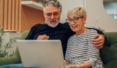 Senior couple leaning towards each other using laptop while sitting on a couch in their home stock photo