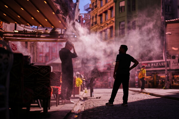 Waiters stand to invite passersby to a restaurant as water is sprayed to cool the area on a hot day in Istanbul, Turkey, Thursday, June 11, 2026. (AP Photo/Francisco Seco)