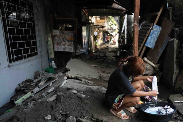 A woman washes clothes along a damaged pathway in General Santos, southern Philippines, Thursday, June 11, 2026, following Monday's powerful earthquake. (AP Photo/Basilio Sepe)