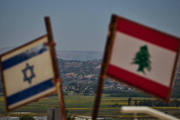 Israeli and Lebanese flags are seen in an area near the border, backdropped by destroyed buildings in southern Lebanon as viewed from northern Israel, Monday, June 15, 2026. (AP Photo/Leo Correa)