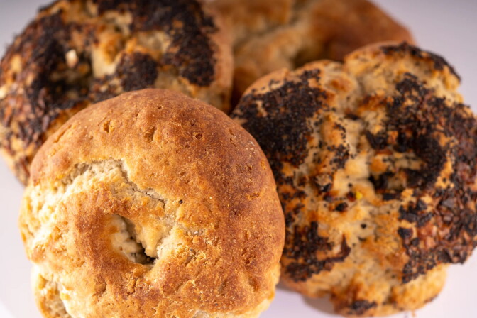 A close up of four bagels, slightly crumbly; two have black poppy seeds on them.