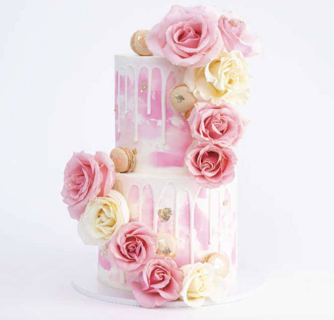 A stunning pink and white cake, with two layers, has pink and white roses cascading down it, with macarons tucked inside.