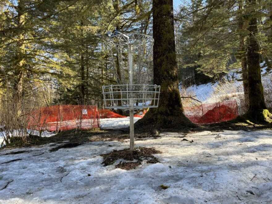 A frisbee golf hole next to the oil spill site during the winter of 2025. A sign on the orange fence reads “CAUTION. OIL RESIDUE PRESENT, PLEASE STAY OUT.”