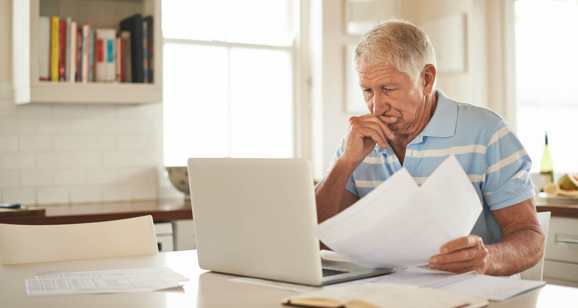 Shot of a senior man looking stressed while doing the household finances on a laptop in his kitchen.