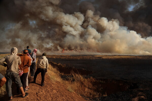 Farmers watch a wildfire burn through agricultural land and wheat fields north of the town of Tal Tamr in al-Hassakeh,province, a key wheat-producing region in northeastern Syria, Thursday, June 18, 2026. (AP Photo/Baderkhan Ahmad)