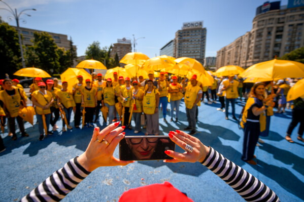 A woman takes a group photo with fellow education-sector union workers outside the Romanian government headquarters during a protest against planned changes to legislation on public-sector salaries in Bucharest, Romania, Wednesday, June 17, 2026. (AP Photo/Alexandru Dobre)