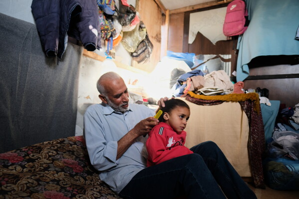 Mahmoud Nofal, 64, combs the hair of his three-year-old granddaughter, Raneen Nofal, whom he has raised since her parents were killed in an Israeli airstrike, in Khan Younis, Thursday, April 30, 2026. (AP Photo/Jehad Alshrafi)